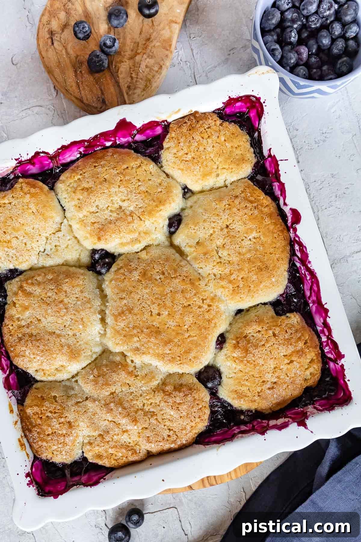 Sweet Summer Blueberry Delight 3 A top-down view of a freshly baked blueberry cobbler in a white baking dish, showing the golden-brown, flaky biscuit topping and the bubbling fruit underneath.