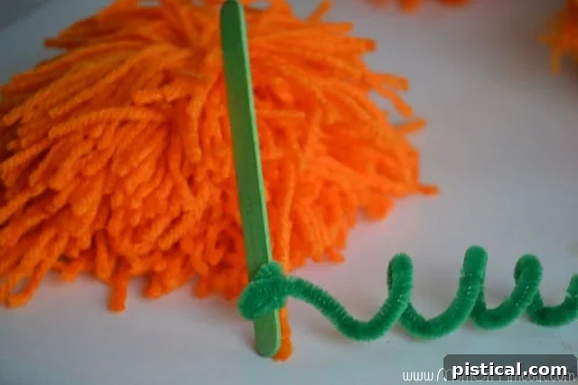 Cute Pom Pom Pumpkins: A Kids Halloween Craft 7 A pipe cleaner wrapped around a popsicle stick to create a stem and vine for a pom pom pumpkin.