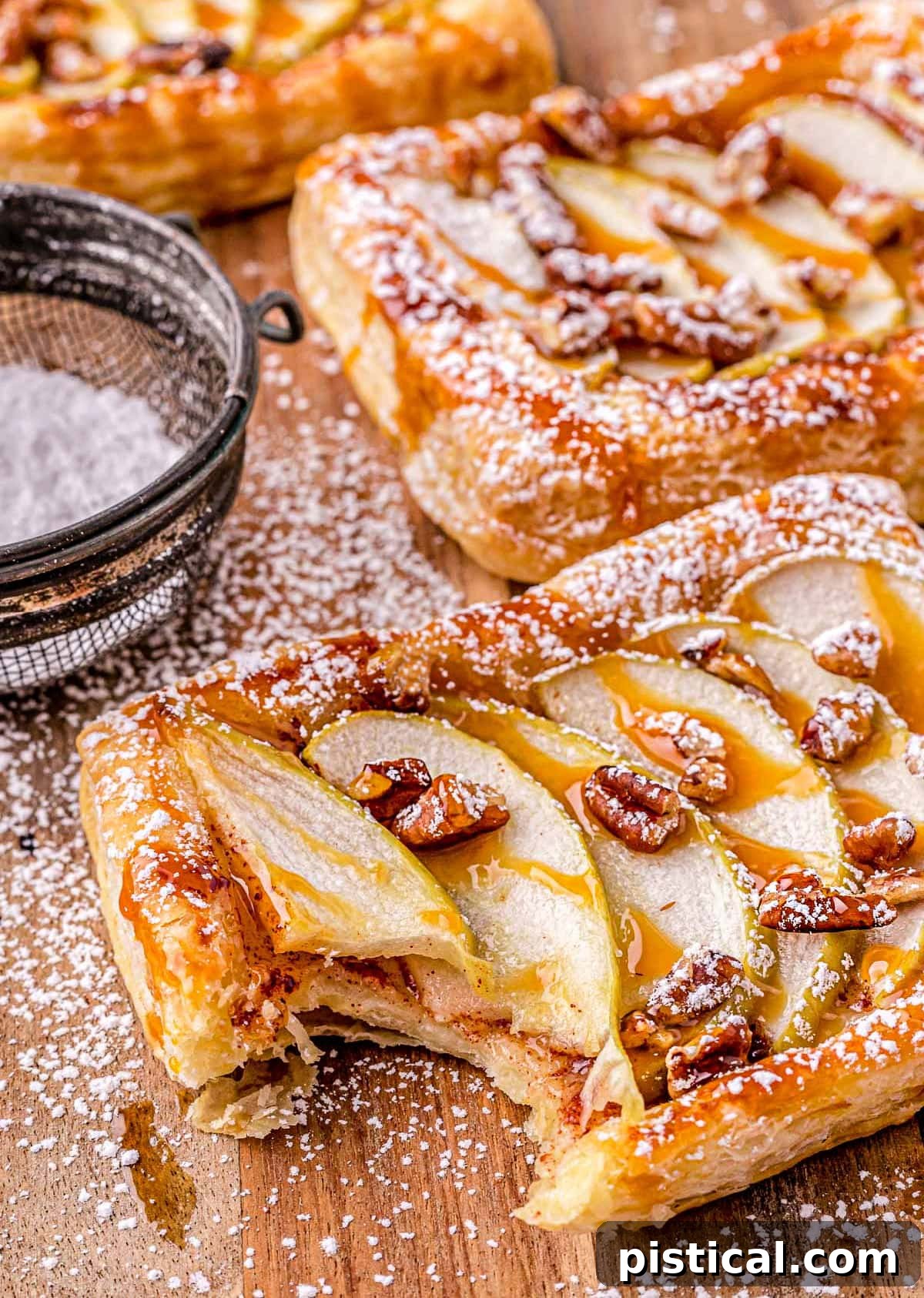 Sweet & Simple Caramel Apple Tart 2 apple tart drizzled with caramel sauce and dusted with powdered sugar on a wood cutting board.