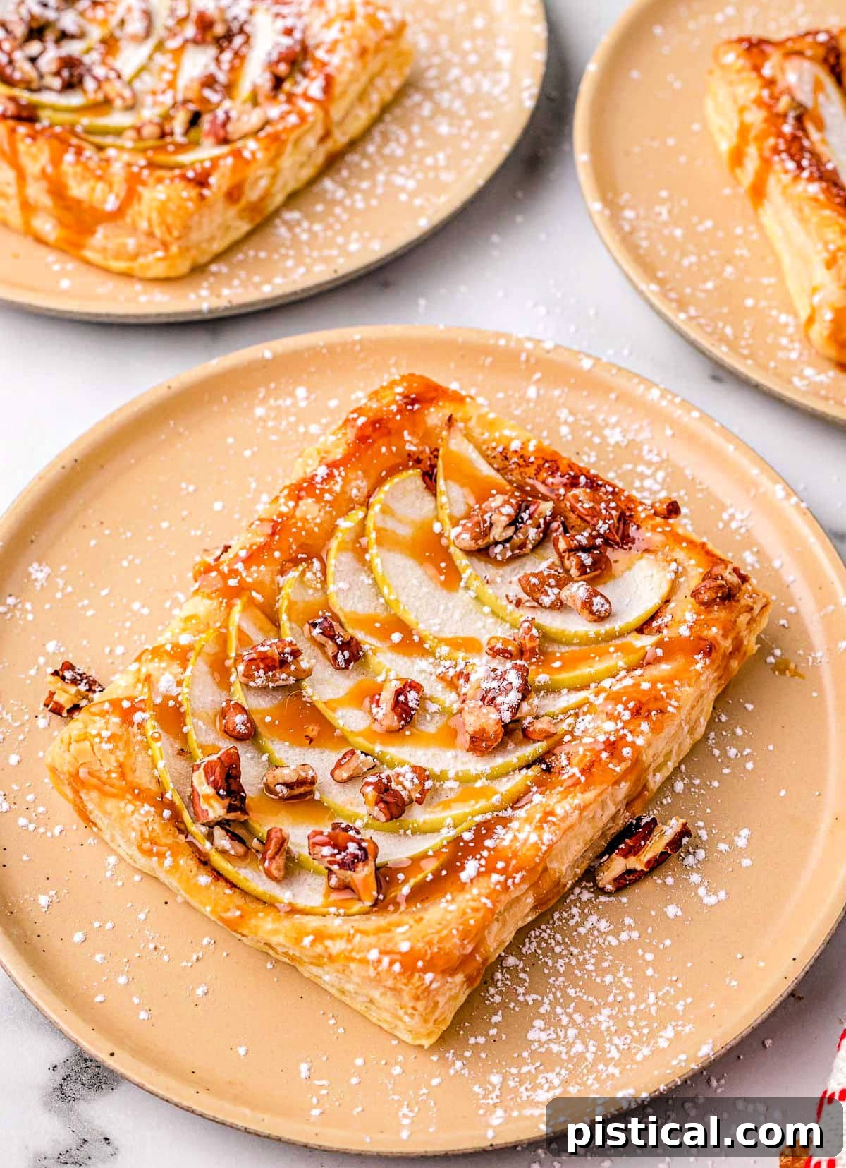 Sweet & Simple Caramel Apple Tart 4 single apple tart on light orange plate with two more apple tarts in the background.