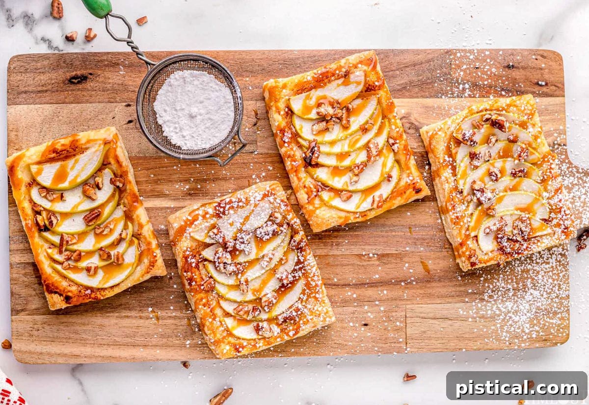 Sweet & Simple Caramel Apple Tart 7 four apple tarts sitting on large wood cutting board drizzled with caramel and sprinkled with powdered sugar.