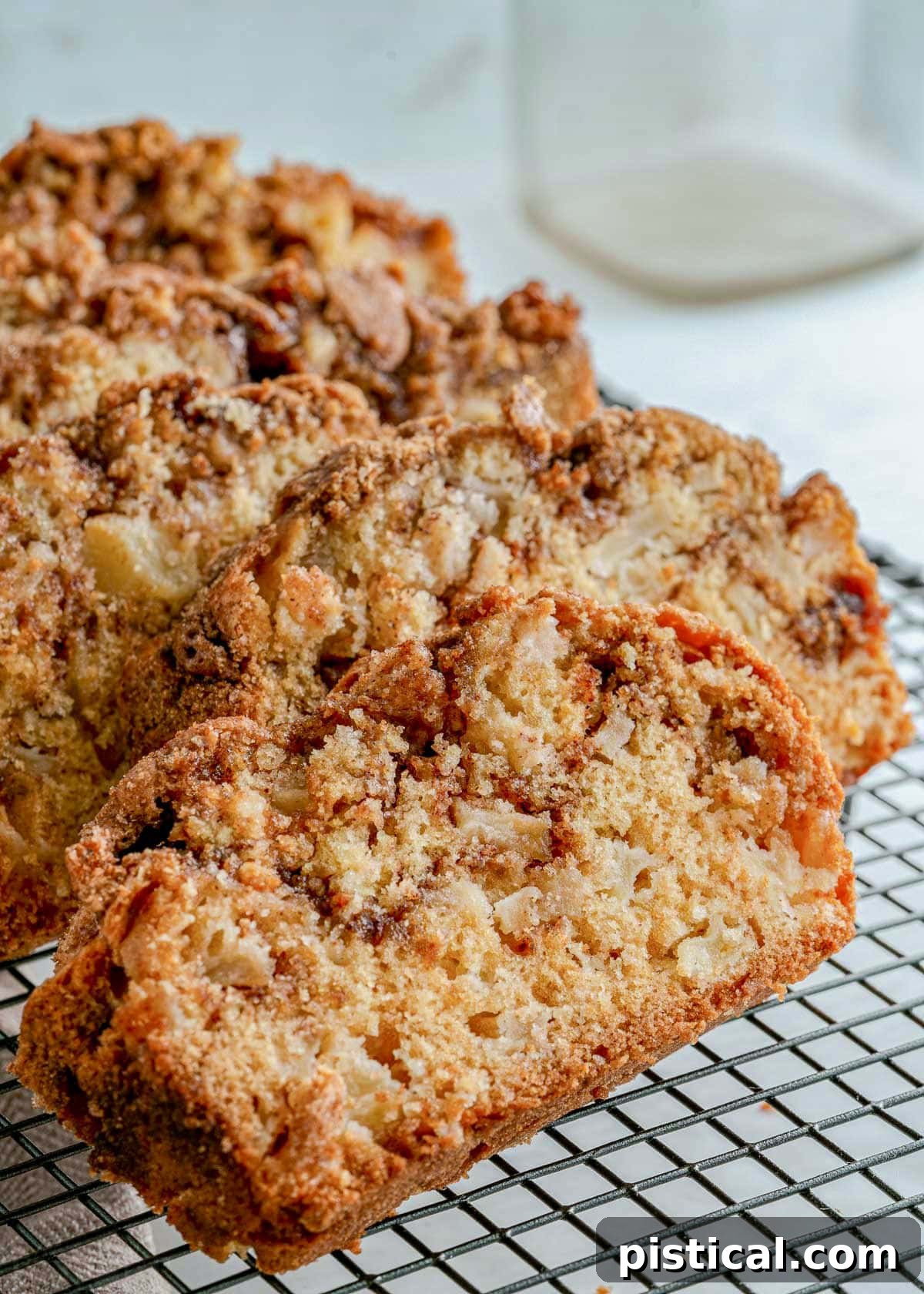 Four golden-brown slices of homemade apple bread cooling on a black wire rack.