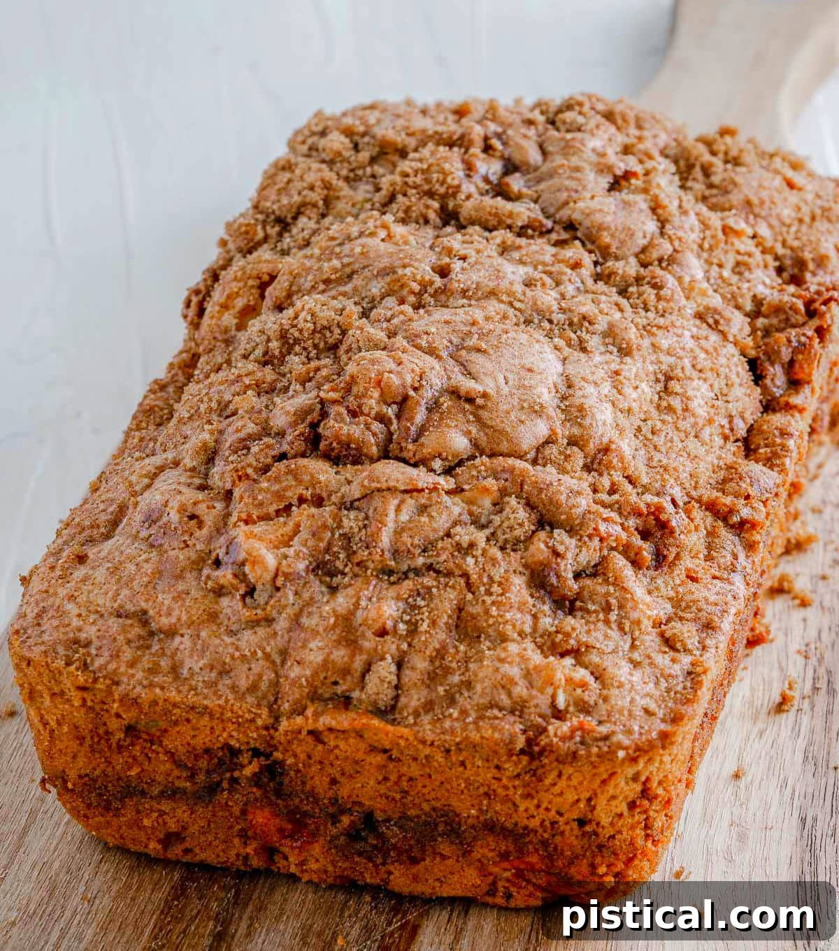 A whole loaf of golden brown apple bread with a visible cinnamon swirl, cooling on a rustic wooden board.