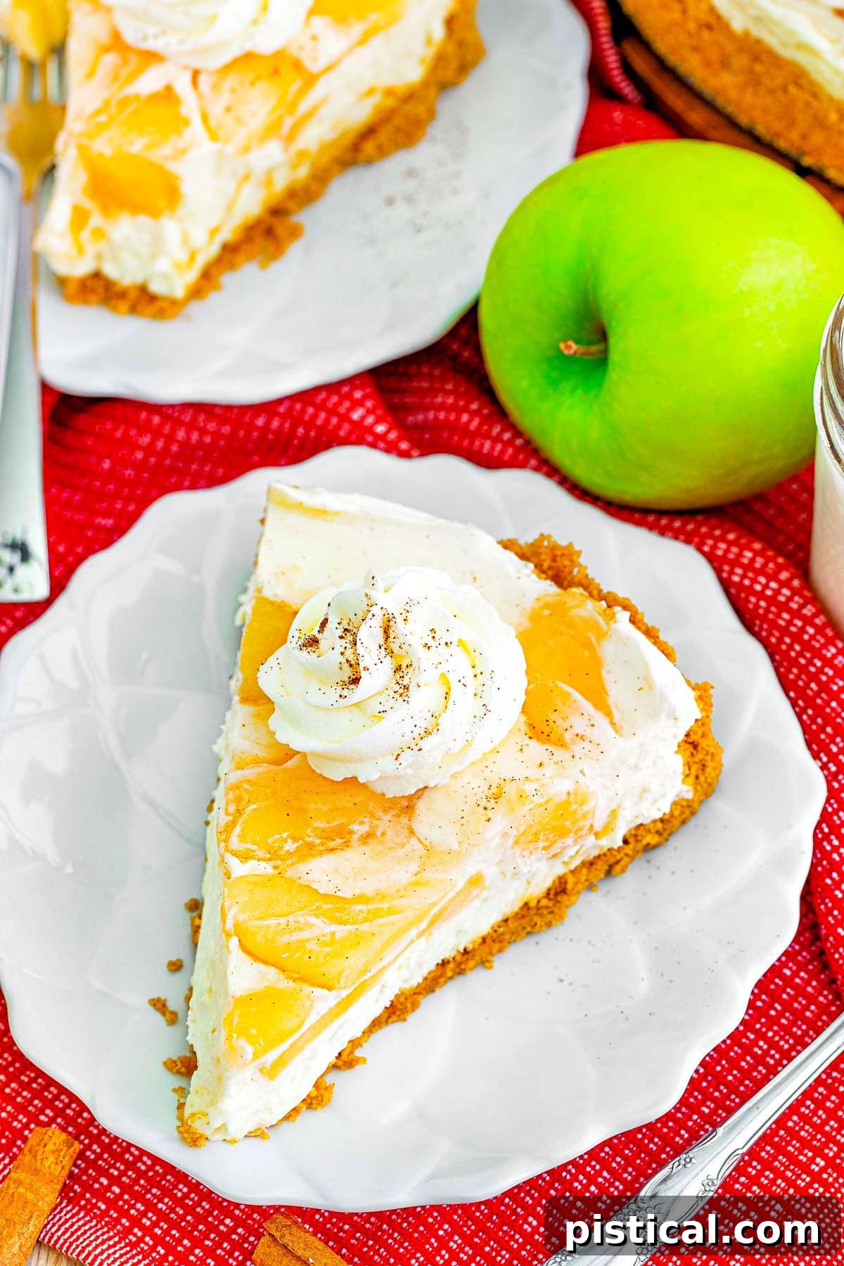An overhead view of a single slice of no bake apple cheesecake on a small white dessert plate, artfully placed beside a fresh Granny Smith apple, highlighting its autumnal charm.