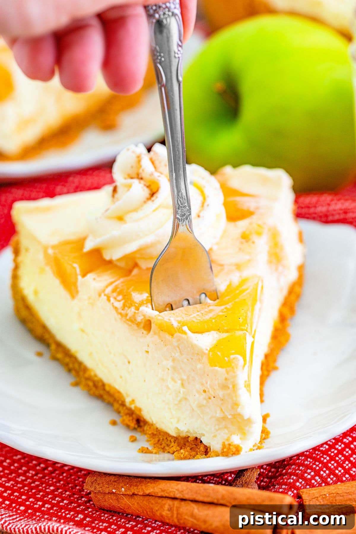 A close-up shot of a perfect slice of no bake apple cheesecake with a fork inserted, ready for a delicious bite, showcasing its creamy texture and apple topping.