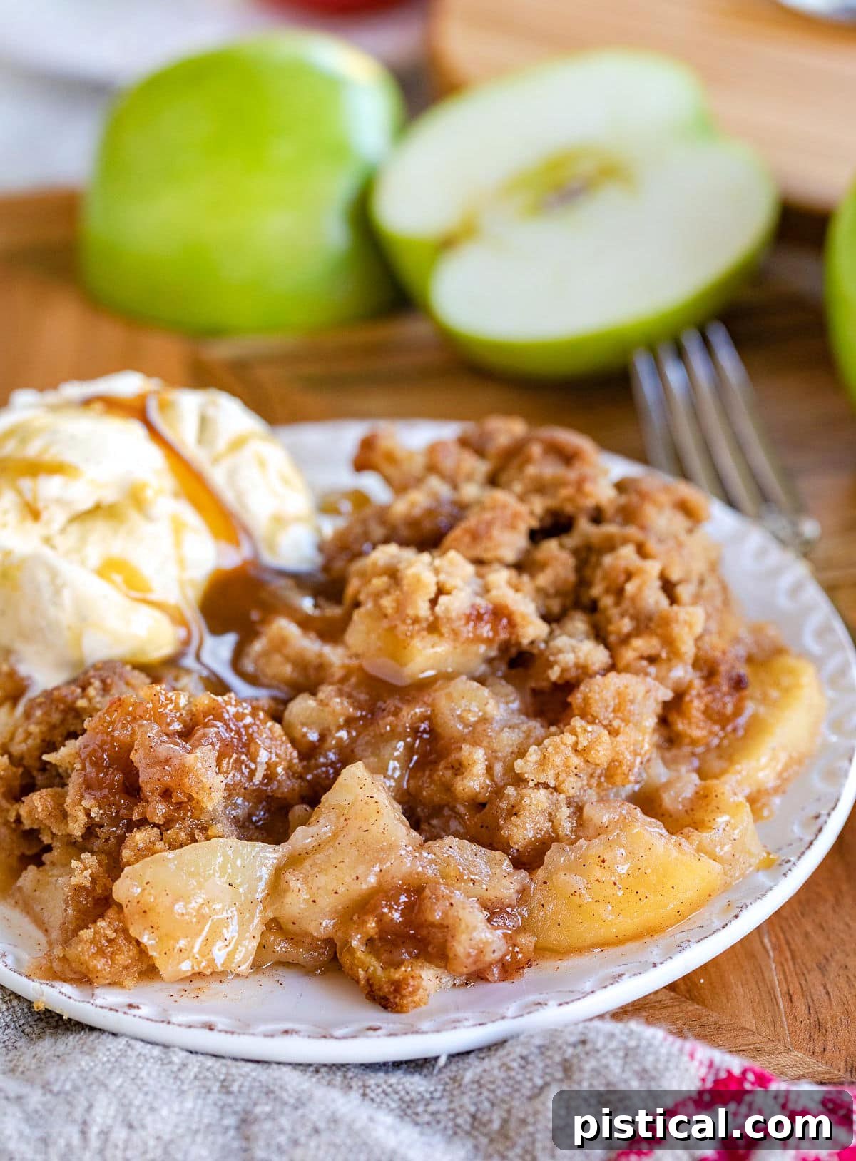 apple crumble served on a small white plate with vanilla ice cream and cut Granny Smith apples in background.