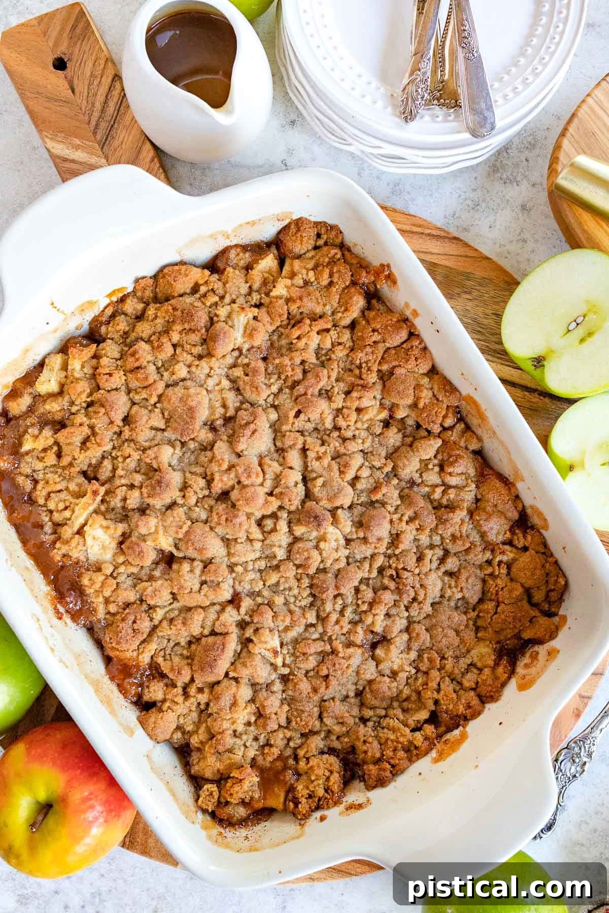top down look at apple crumble in white baking dish sitting on wood cutting board.