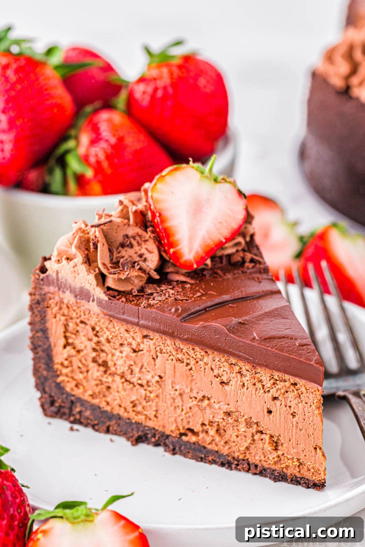 Slice of decadent chocolate cheesecake with an oreo crust and rich chocolate ganache on white round plate. Topped with chocolate shavings and fresh strawberries.