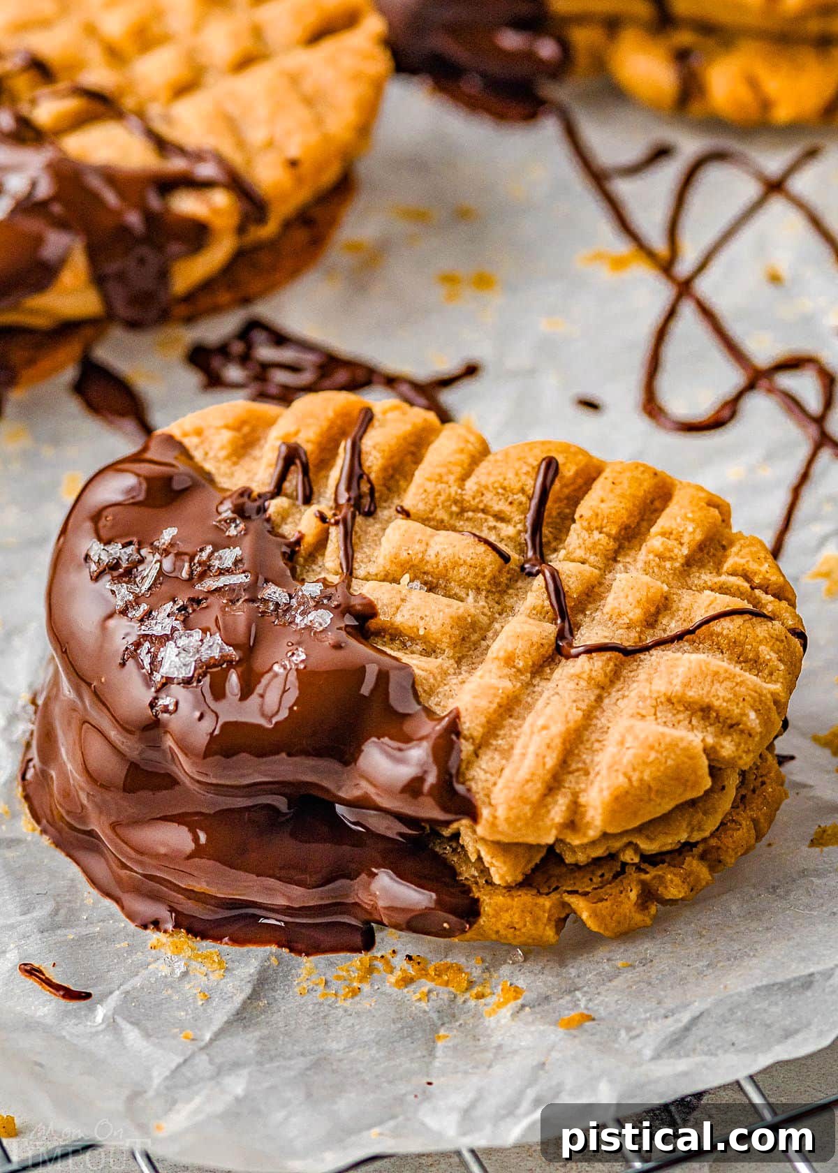 single nutter butter cookie dipping in dark chocolate and sprinkled with sea salt sitting on parchment paper while the chocolate sets up.