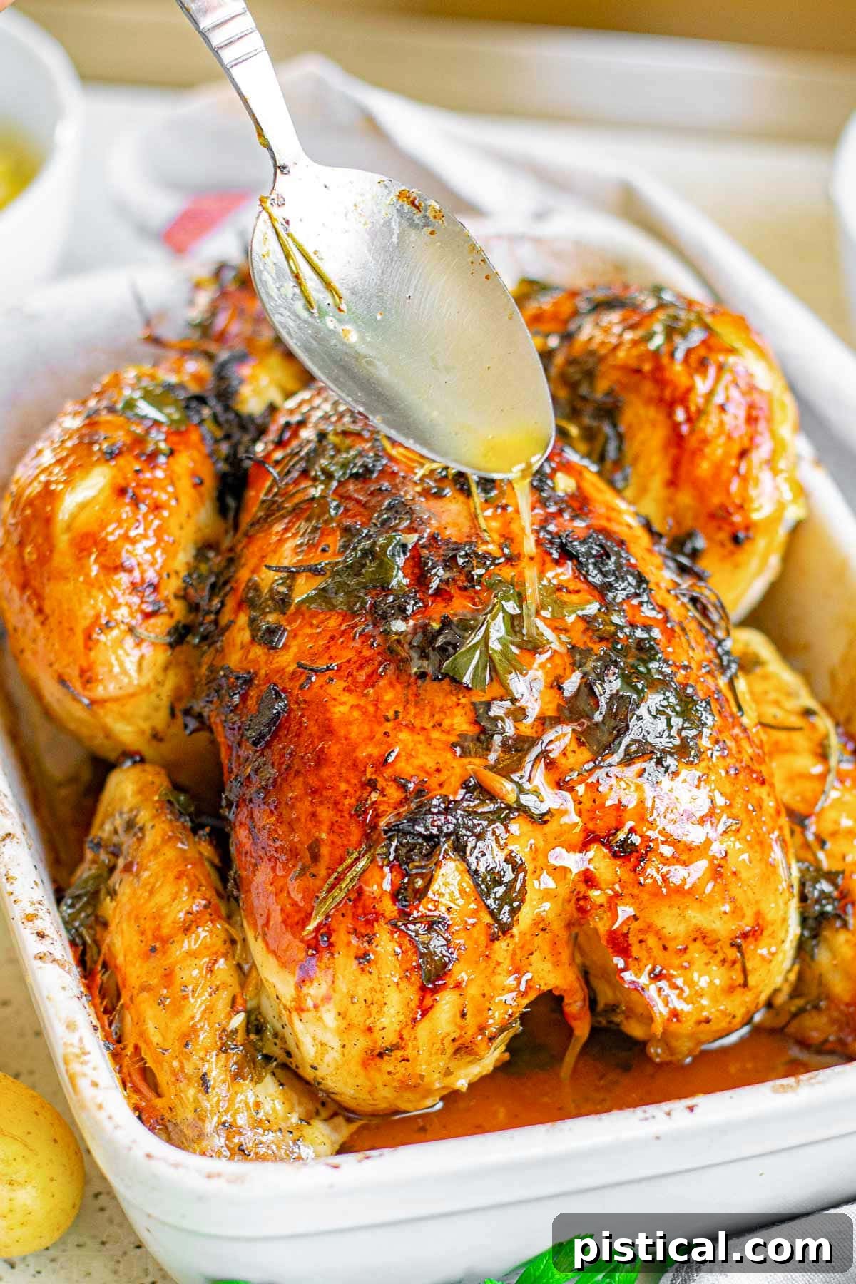 whole roasted chicken in baking dish with spoonful of pan juices being drizzled on top of the whole chicken.