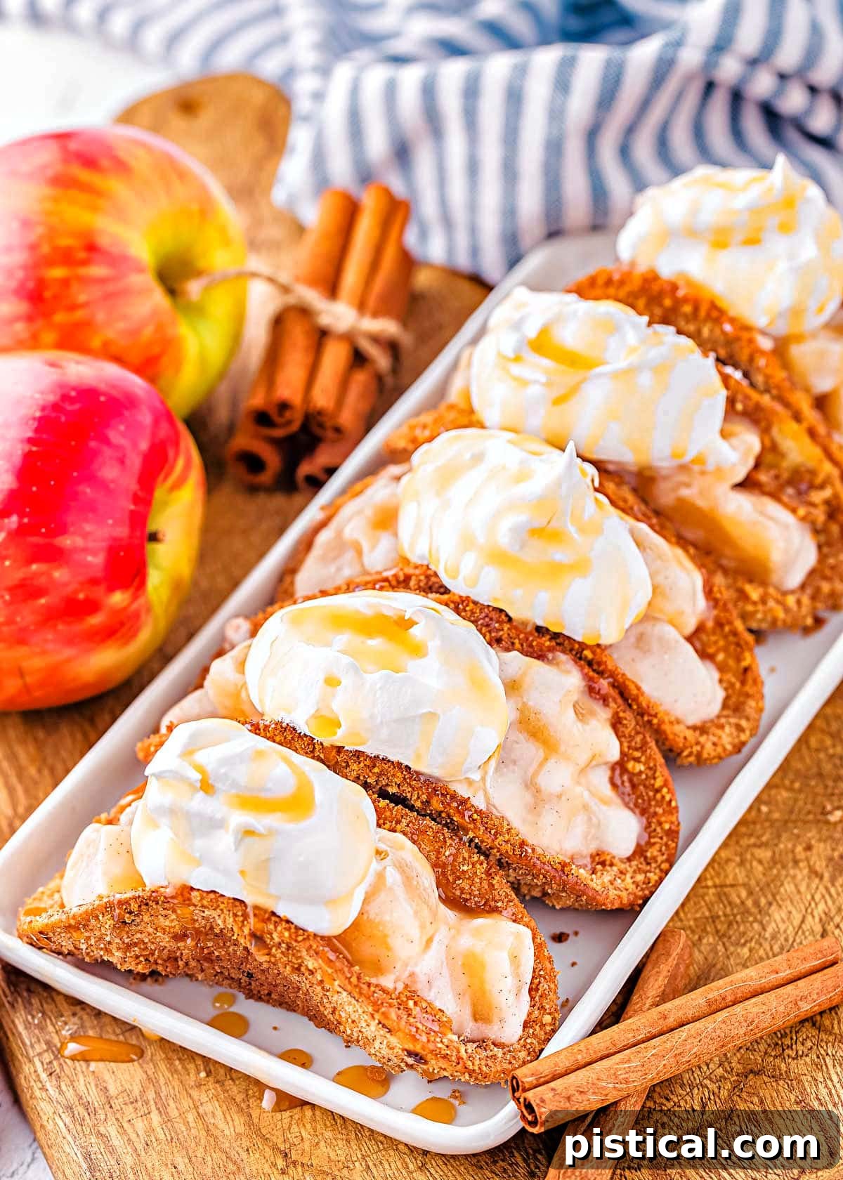 Cinnamon Apple Taco Treats 2 5 apple pie tacos on shallow white serving dish sitting next to blue and white striped napkin and fresh red apples.