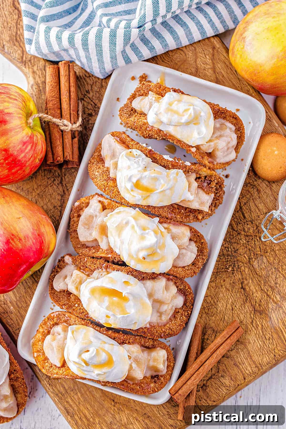 Cinnamon Apple Taco Treats 3 top down view of dessert tacos filled with apple pie filling and topped with whipped cream and caramel all lined up on a white tray ready to serve.