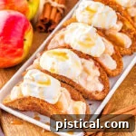 Cinnamon Apple Taco Treats 6 5 apple pie tacos on shallow white serving dish sitting next to blue and white striped napkin and fresh red apples.