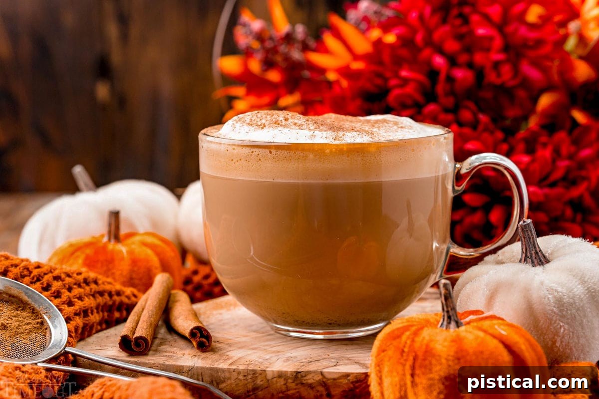 Harvest Spice Latte 3 Front view of a pumpkin spice latte ready to be enjoyed garnished with pumpkin pie spice and sitting in front of fall colored flowers on a wood board.
