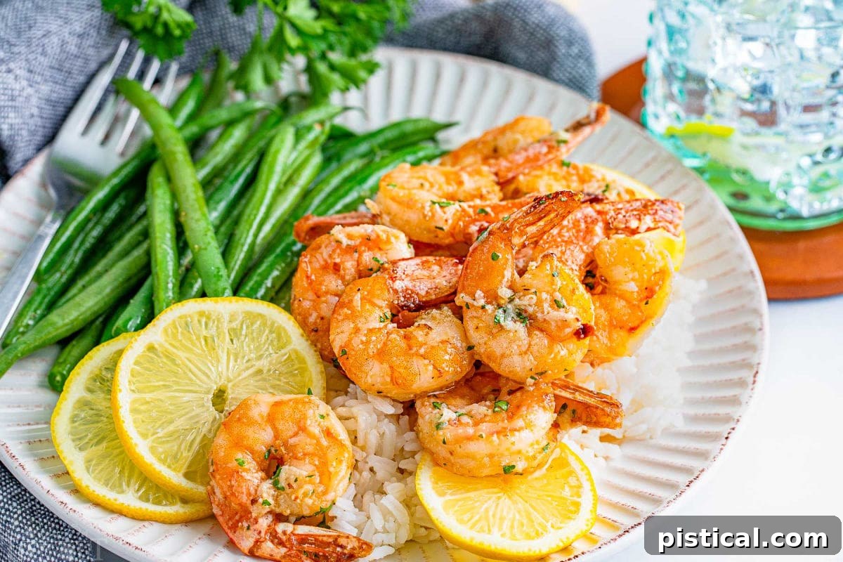 Air fried garlic butter shrimp served on an elegant white scalloped plate, accompanied by vibrant green beans and bright lemon wedges.