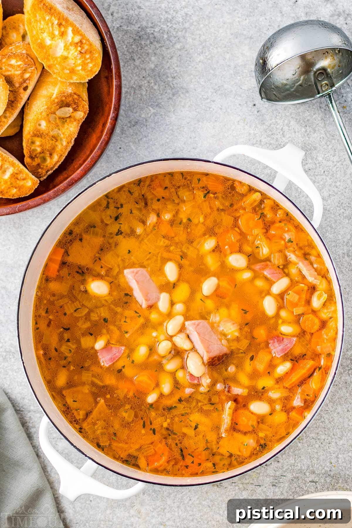 pot full of ham and bean soup with crusty bread in upper left corner on plate.