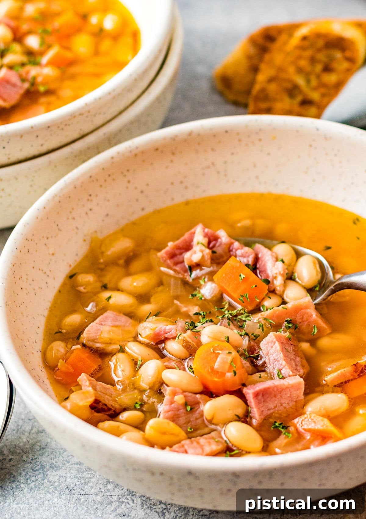 bowl full of ham and bean soup with lots of broth and a spoon.