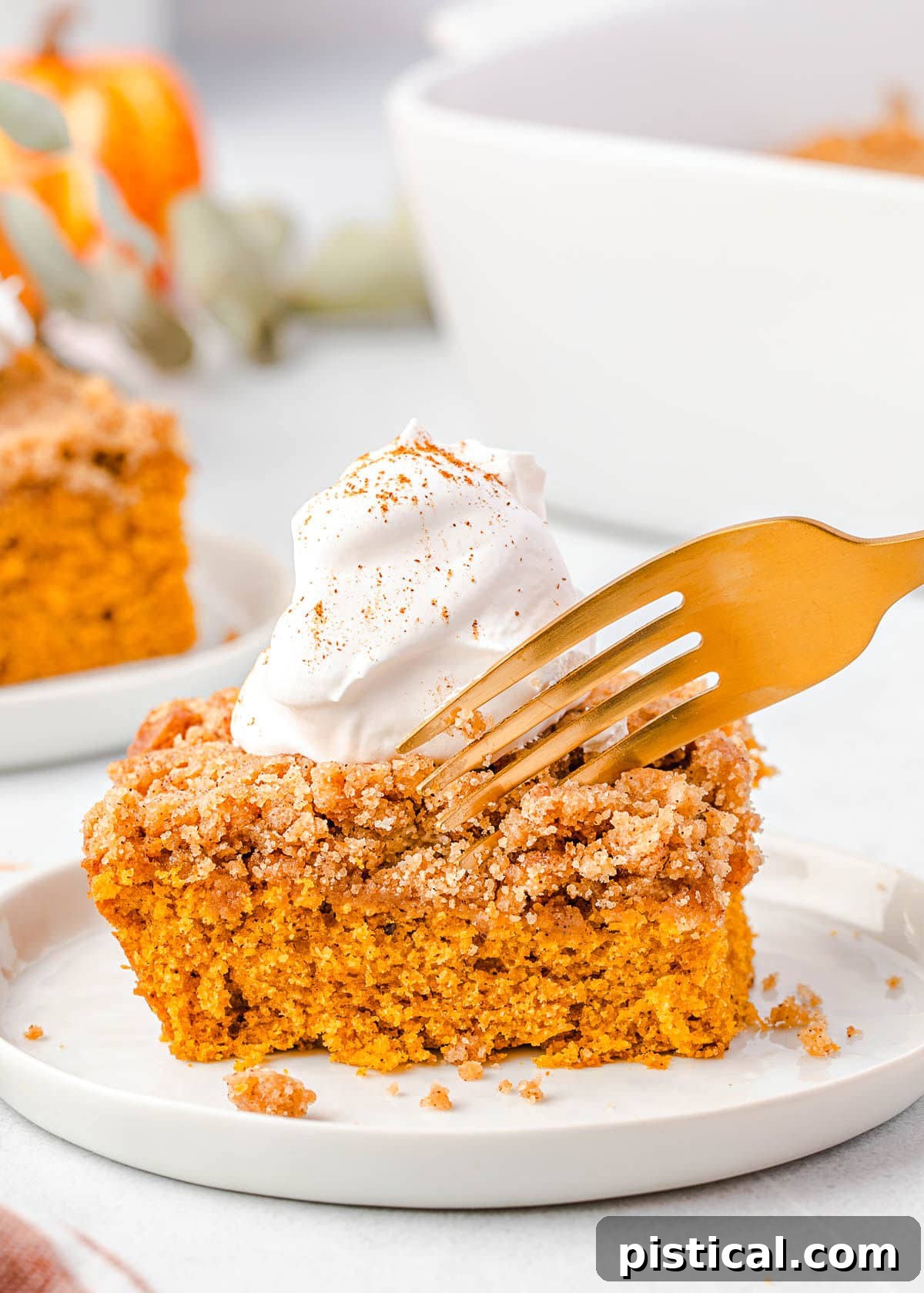 A fork is poised to take a delicious bite of moist pumpkin cake, adorned with a generous swirl of whipped cream on top, highlighting its irresistible texture.