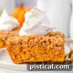 piece of pumpkin coffee cake sitting on stack of white plates topped with whipped cream
