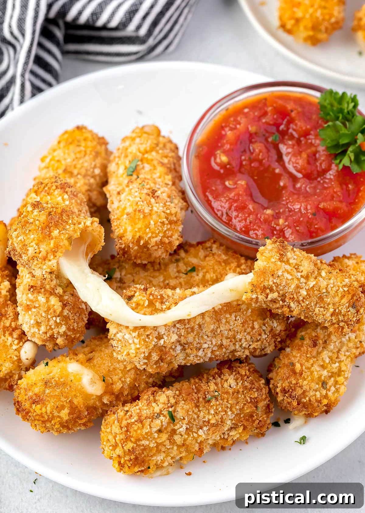 Golden & Gooey Air Fryer Mozzarella Sticks 7 A perfectly cooked mozzarella stick displaying an impressive, long cheese pull, resting atop a bed of other crispy mozzarella sticks on a white plate, invitingly presented.