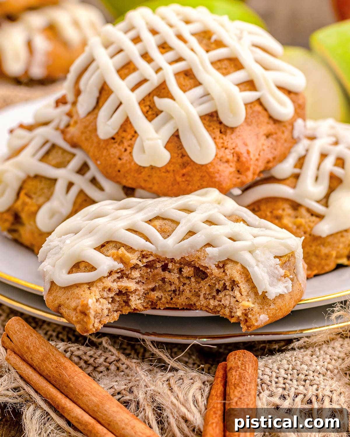 A small white plate holds several apple cookies, one with a bite taken out, all generously drizzled with maple icing.