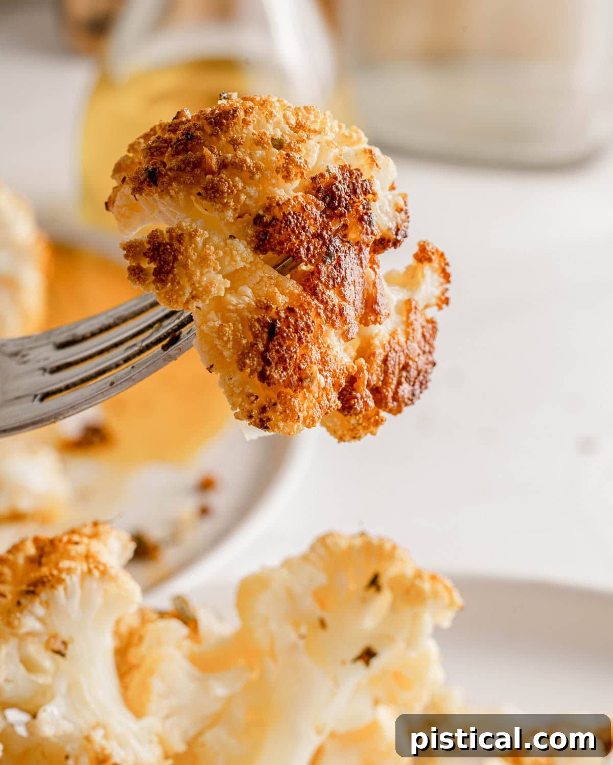 A perfectly roasted piece of cauliflower, golden brown and tender, is delicately held on a fork, ready to be enjoyed.