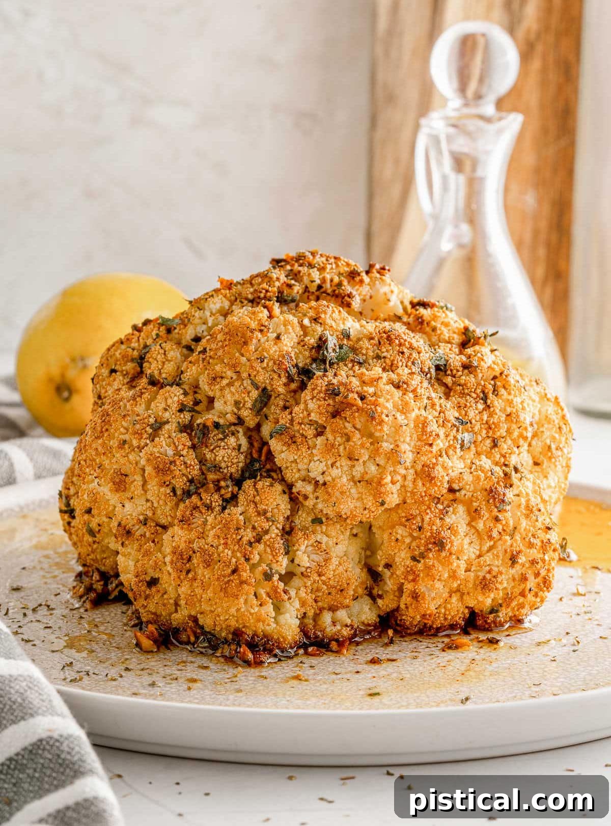 A whole roasted cauliflower, beautifully golden and seasoned, presented on a white plate, ready to be carved and enjoyed.