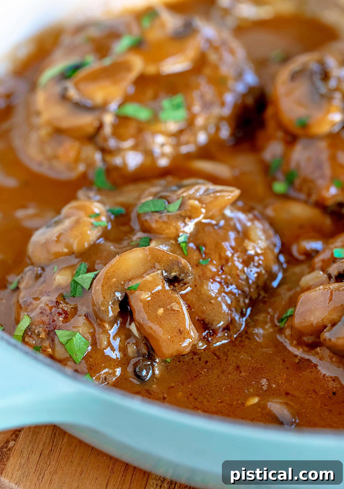 four salisbury steaks in large skillet with mushroom gravy and fresh parsley sprinkled over the top of them.