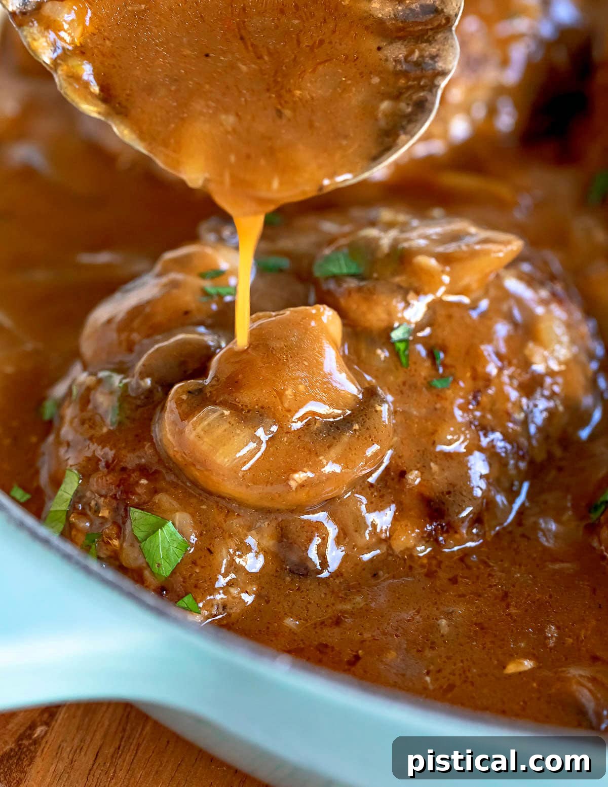 gravy being poured onto a salisbury steak still in the skillet.