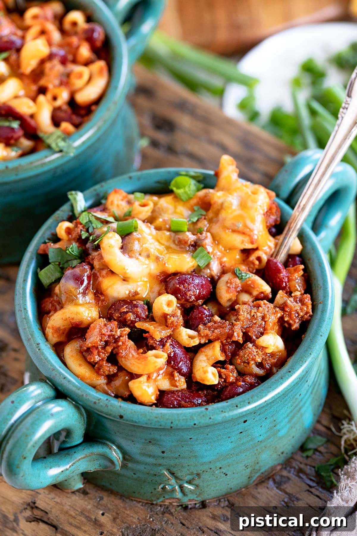 teal bowl filled with chili mac and topped with shredded cheese and sliced green onions.