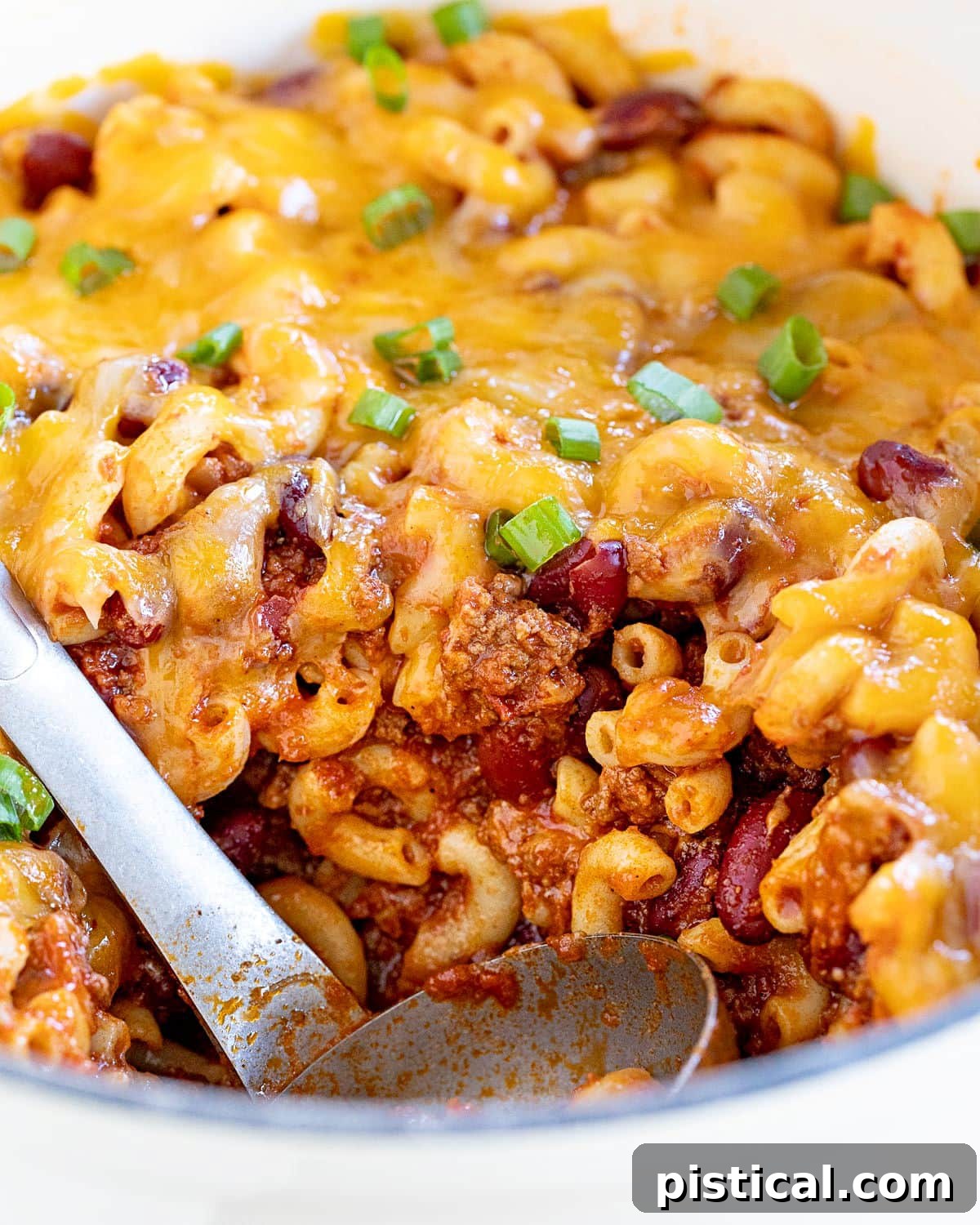 scoop of chili mac removed from large white dutch oven.
