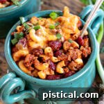 teal bowl filled with chili mac and topped with shredded cheese and sliced green onions.