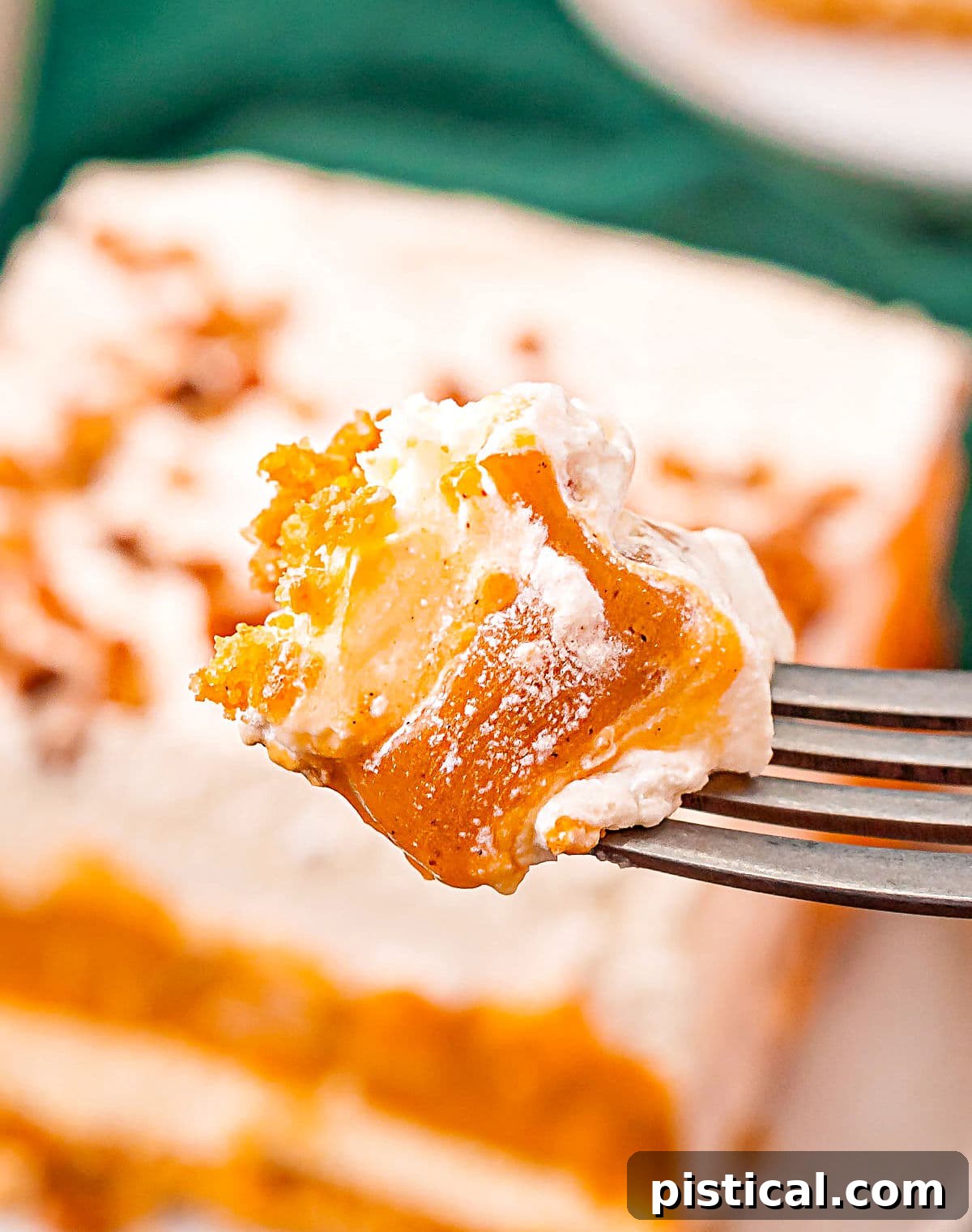 A fork holds a perfect bite of layered pumpkin delight dessert, with the rest of the dessert artfully blurred in the background, ready for enjoyment.