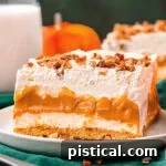 Four layer pumpkin dessert sitting on white plate topped with pecans and pumpkin pie spice.