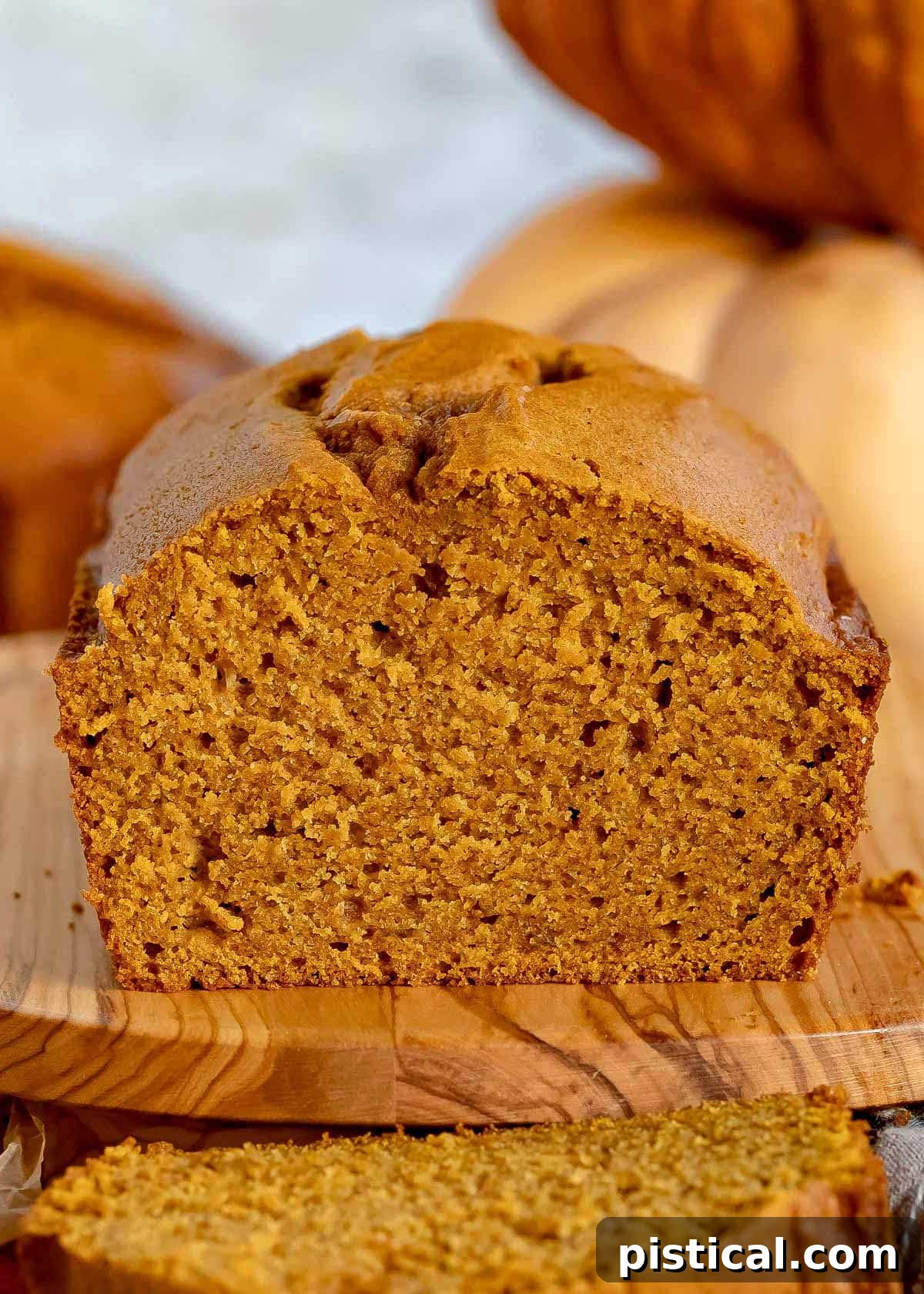 Ultimate Pumpkin Bread 2 A golden-brown loaf of homemade pumpkin bread rests on an olive wood cutting board, with one perfect slice cut and ready to enjoy.
