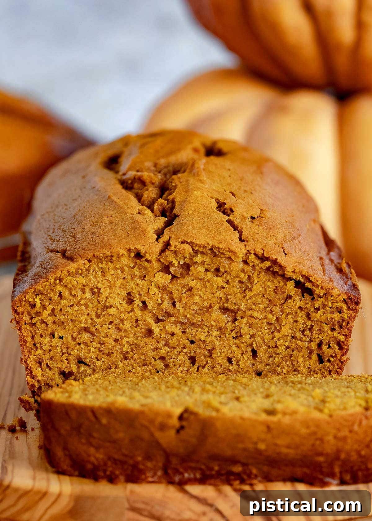 Ultimate Pumpkin Bread 4 A golden-brown loaf of pumpkin bread on a rustic wooden board, with a single slice removed and positioned to highlight its soft texture.