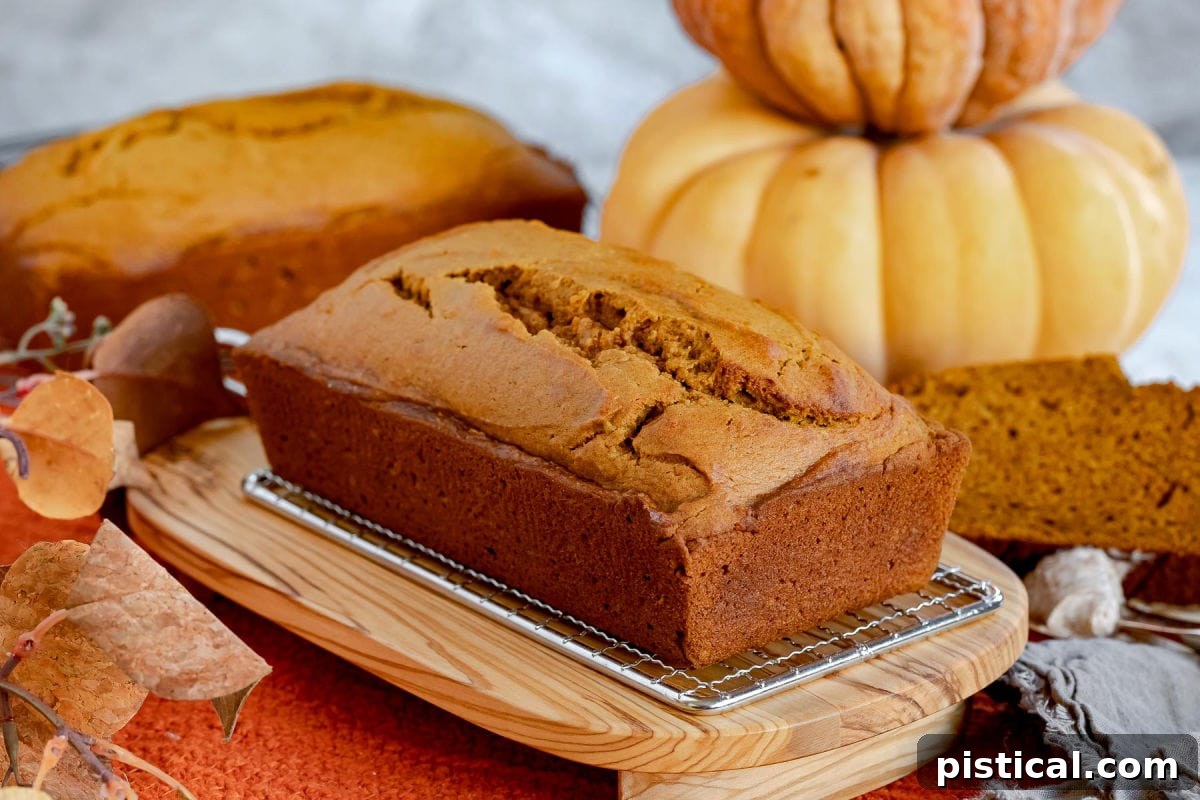 Ultimate Pumpkin Bread 5 Two perfect loaves of pumpkin bread, one whole and one partially sliced, are presented on an olive wood board against a rustic background.