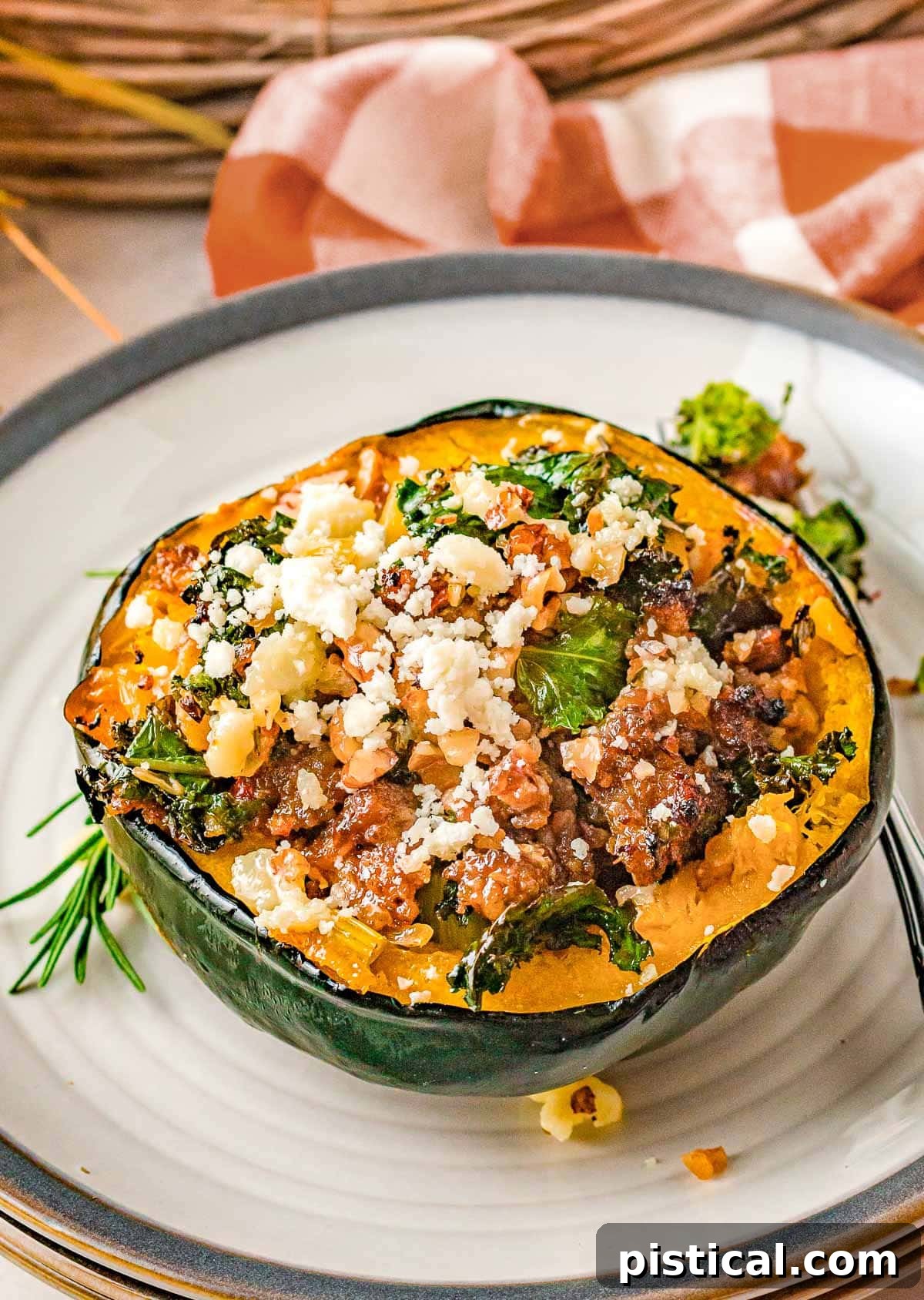 Half of an acorn squash stuffed with a savory sausage and veggie mixture, resting on a white plate with a gray rim.