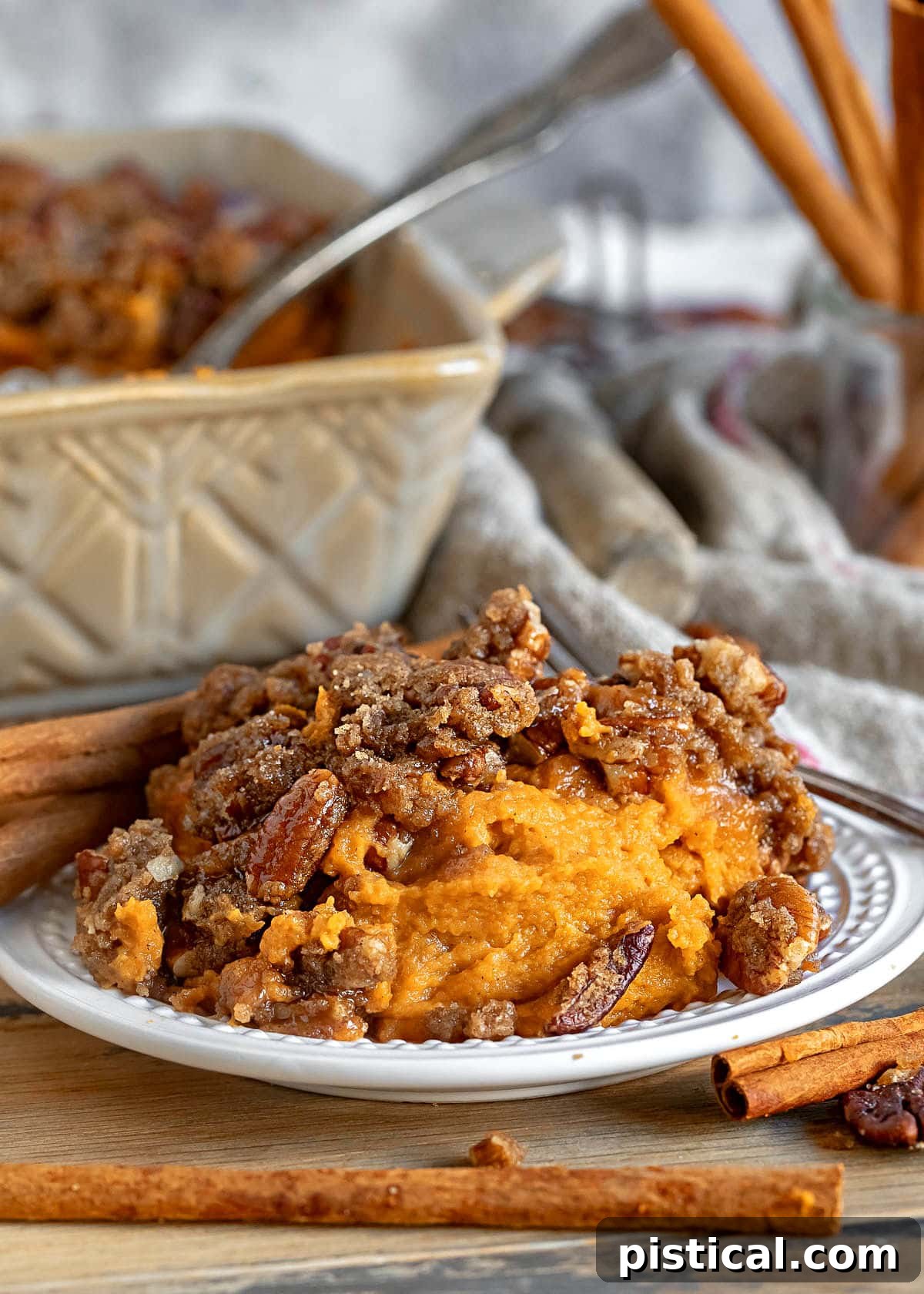 A small plate showcasing a serving of sweet potato casserole, topped with a generous pecan streusel. In the background, the full baking dish sits, ready for more.