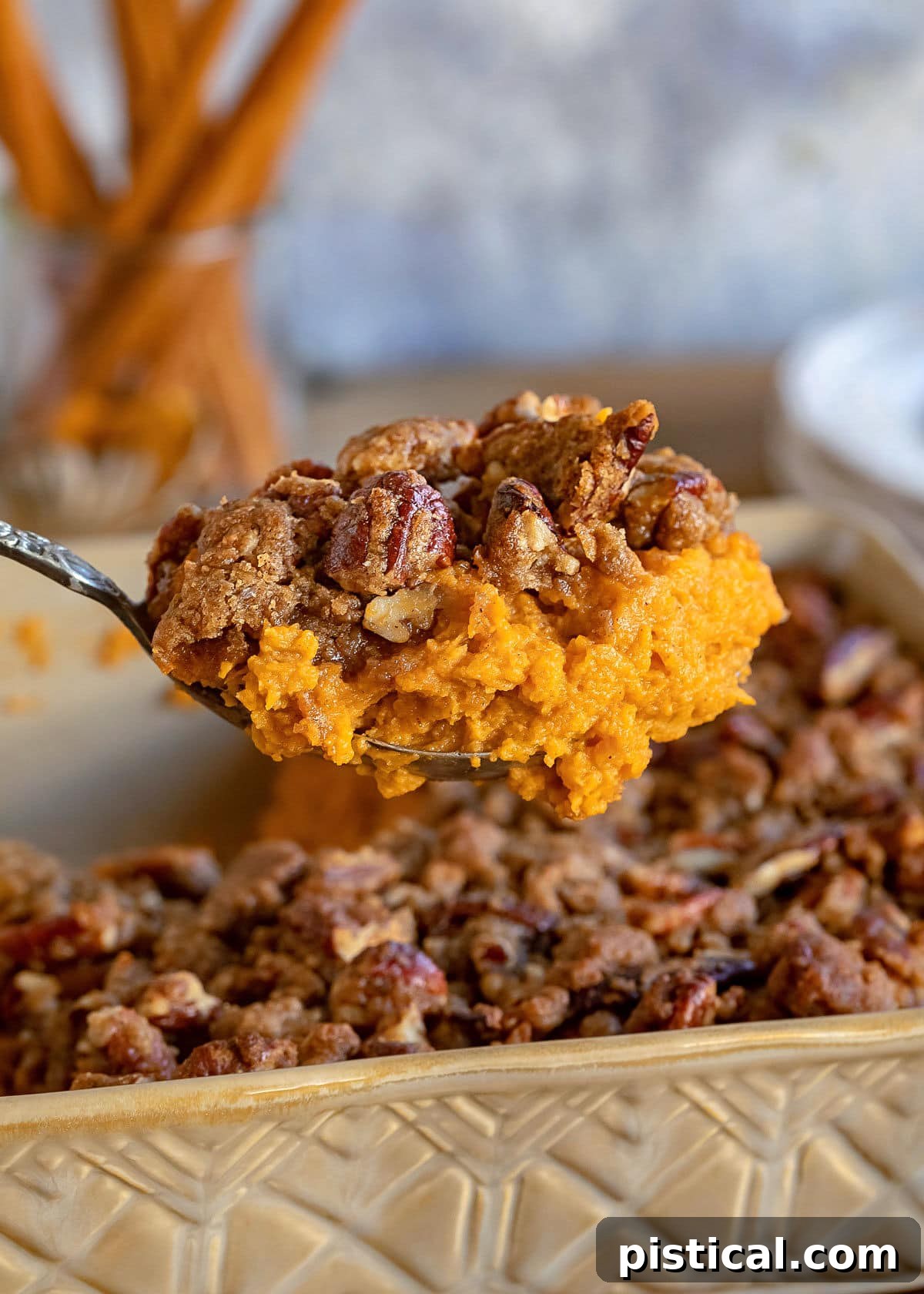A large serving spoon lifts a generous scoop of the golden-brown sweet potato casserole, revealing its creamy texture beneath the crunchy topping.