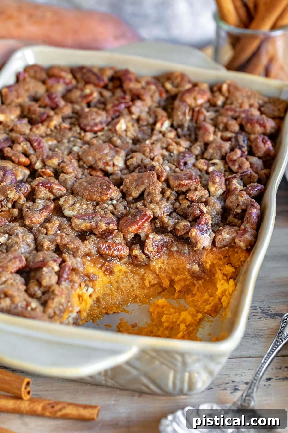 A serving dish of sweet potato casserole with a scoop removed, highlighting its rich interior and streusel topping, indicating it's ready to be enjoyed.