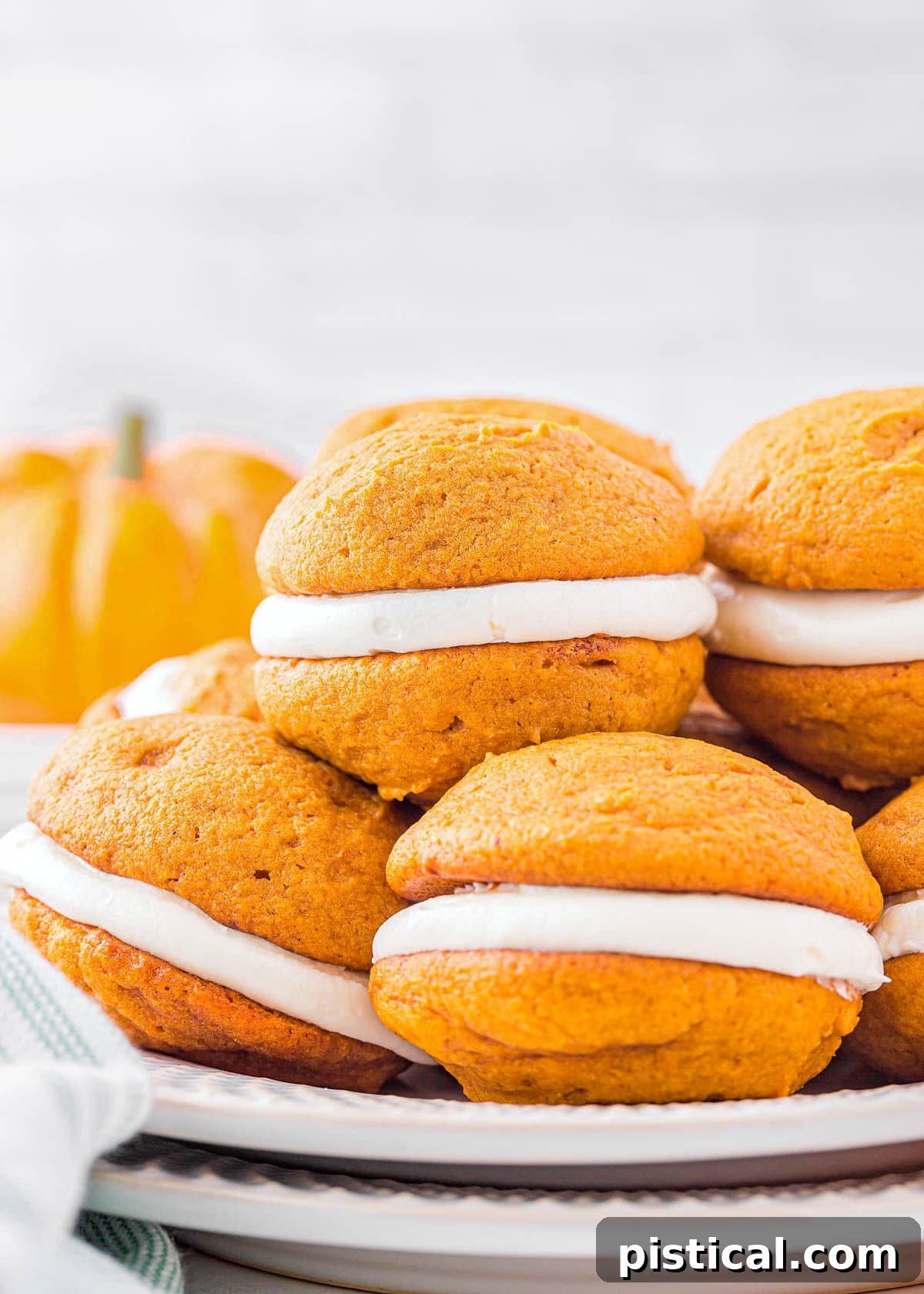 A beautifully arranged plate featuring six golden-orange pumpkin whoopie pies, each perfectly stacked and inviting. The fluffy pumpkin cookies are generously filled with creamy white frosting, making them an irresistible holiday dessert.