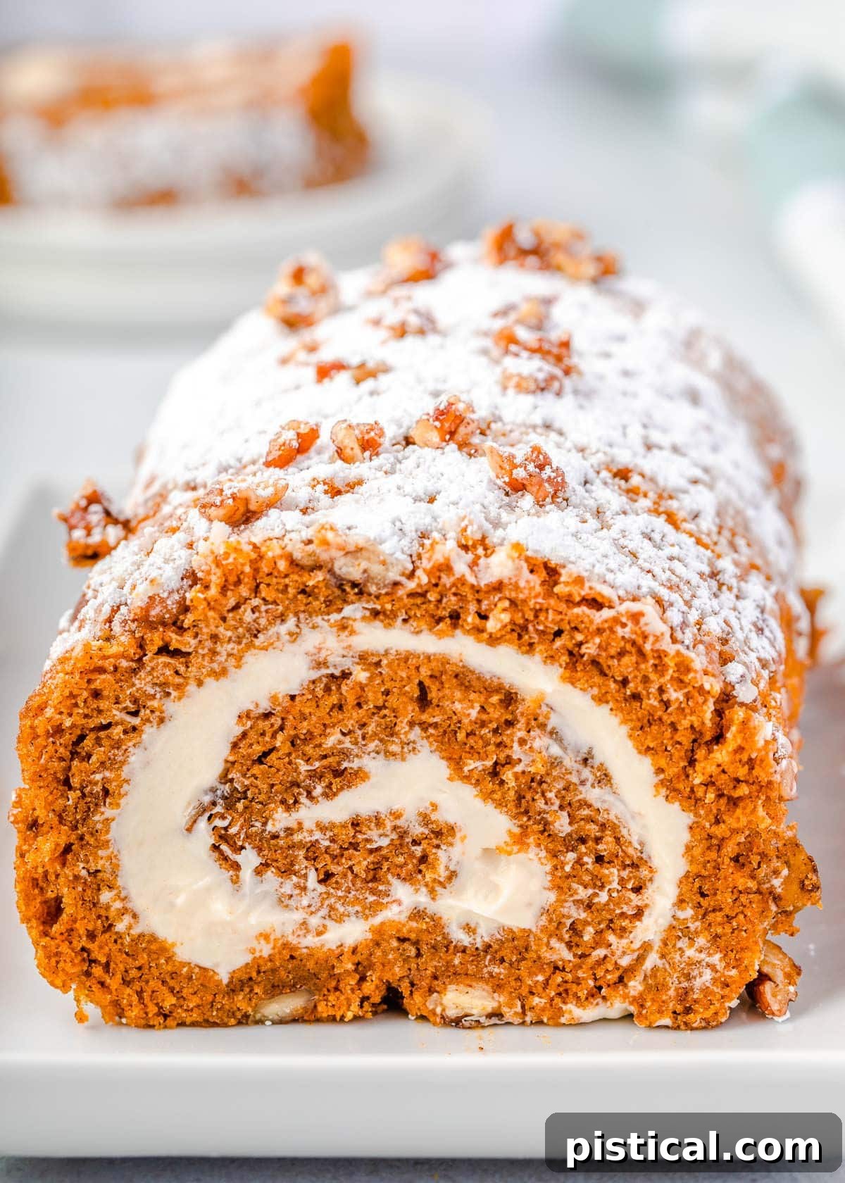 pumpkin roll with candied pecans sitting on long white tray dusted with powdered sugar. 