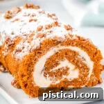 whole pumpkin cake roll on a white rectangle plate with powdered sugar and candied pecans on top of the cake roll.