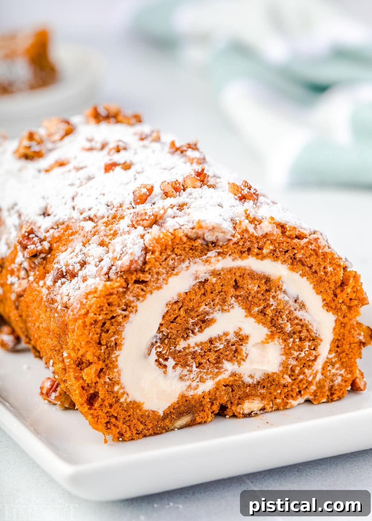 whole pumpkin cake roll on a white rectangle plate with powdered sugar and candied pecans on top of the cake roll.