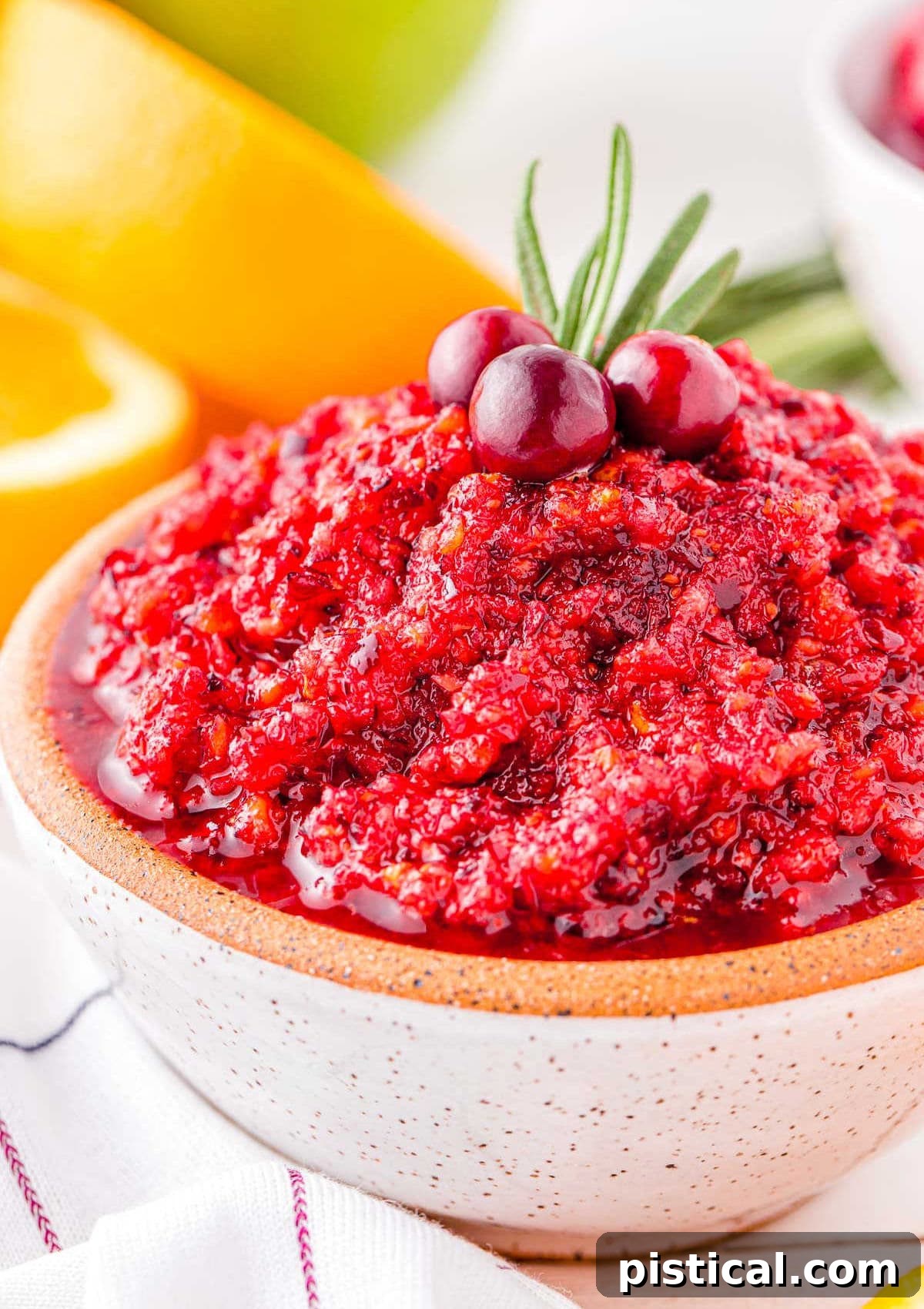 bowl of cranberry relish made with oranges and apples in a small white bowl topped with rosemary and fresh cranberries.