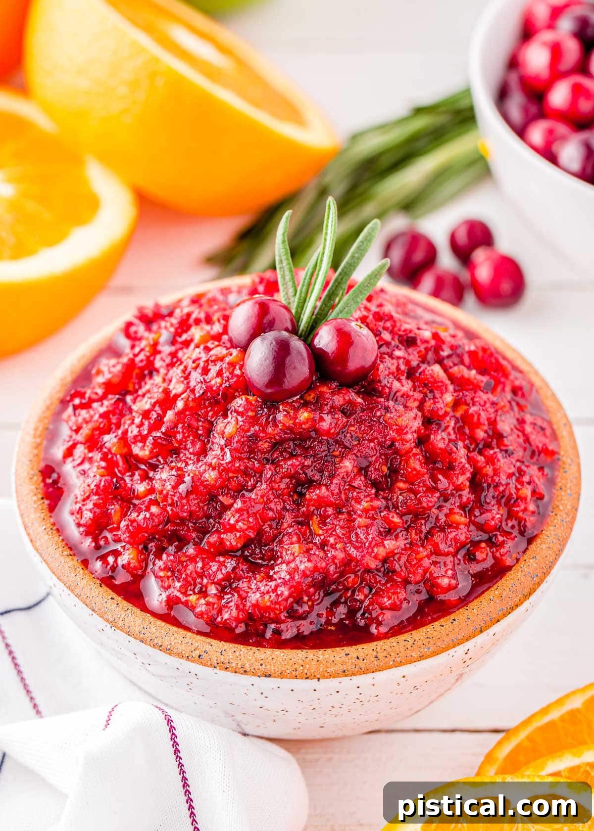 beautiful bowl of bright cranberry relish topped with a sprig of rosemary and three fresh cranberries.