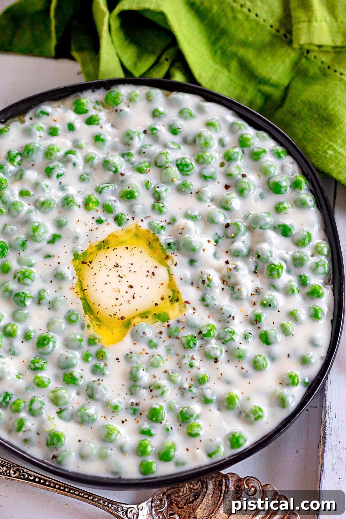 Top-down view of creamed peas served in a stylish black bowl, adorned with melted butter and a generous sprinkle of freshly cracked black pepper, highlighting its inviting warmth.