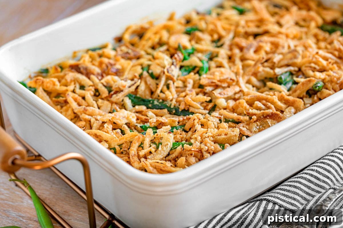 A tempting side view of the finished green bean casserole, generously topped with golden fried onions, presented in a large white casserole dish, ready to be served and enjoyed.