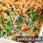Green bean casserole in a large white baking dish topped with fried onions. Two silver serving spoons are in the dish with a serving or two removed.